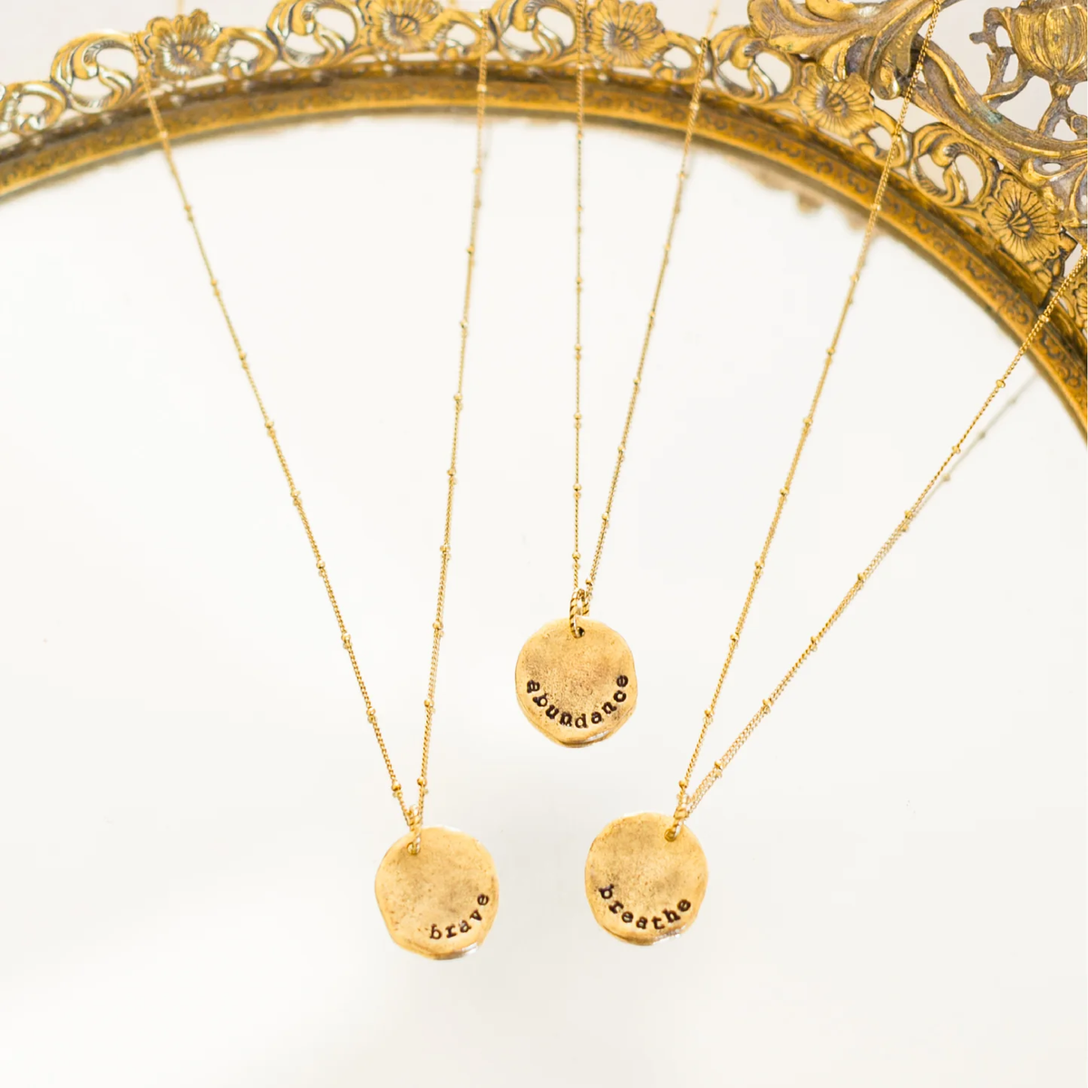 Three gold hand-stamped disc pendants reading abundance, brave and breathe